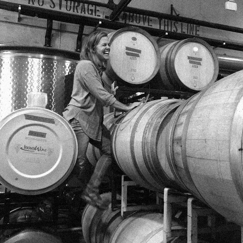 Lynn standing on some barrels in the winery laughing while at work